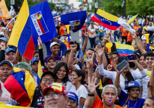 A crowd holds signs and Venezuela flags at a rally